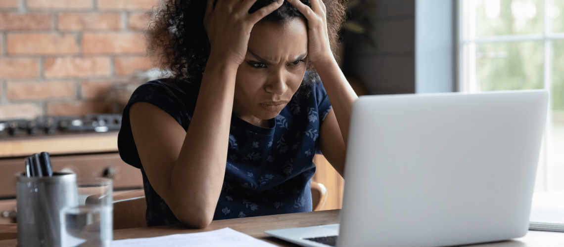 Website Woman holding her head in her hands looking frustrated at her laptop